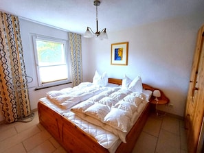 A bedroom with a wooden bed, a window with curtains, a painting on the wall, and a bedside lamp. - Feriendomizile auf der Insel Poel (Insel Poel)