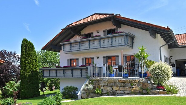 A two-story house with a balcony, stone foundation, and a well-maintained garden. - Ferienwohnung im Bayerischen Wald mit Whirlpool (Waldkirchen)