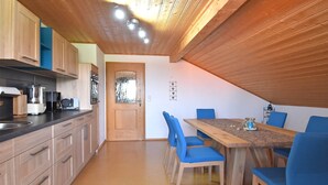 A kitchen with wooden cabinets, a dining table with blue chairs, and a wooden ceiling. - Ferienwohnung im Bayerischen Wald mit Whirlpool (Waldkirchen)