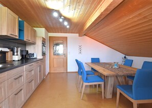 A kitchen with wooden cabinets, a dining table with blue chairs, and a wooden ceiling. - Ferienwohnung im Bayerischen Wald mit Whirlpool (Waldkirchen)