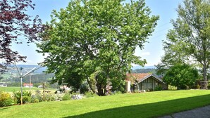 A rural landscape with a large tree, a stone house, and a paved path. - Ferienwohnung im Bayerischen Wald mit Whirlpool (Waldkirchen)
