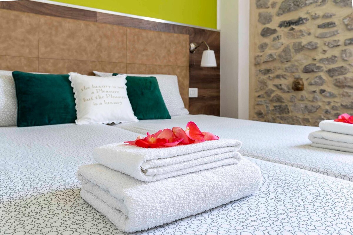 A neatly made bed with folded white towels and a decorative flower, a wooden headboard, and a stone wall.
