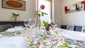 Una mesa de comedor dispuesta con platos blancos, vasos transparentes y un florero con una rosa rosa.