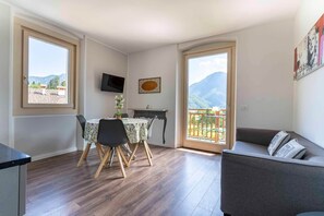 A modern living room with a dining area, a sofa, and a TV mounted on the wall. - Apartment in Mezzolago by Lake Ledro (Ledro)