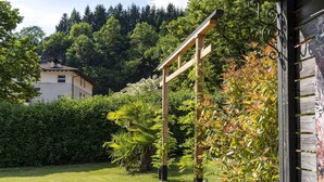 Ein Garten mit einer Holzpergola, üppigem Grün und einem Gebäude im Hintergrund.