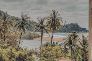 Blick auf einen Strand mit Palmen und einer felsigen Hügelkulisse.