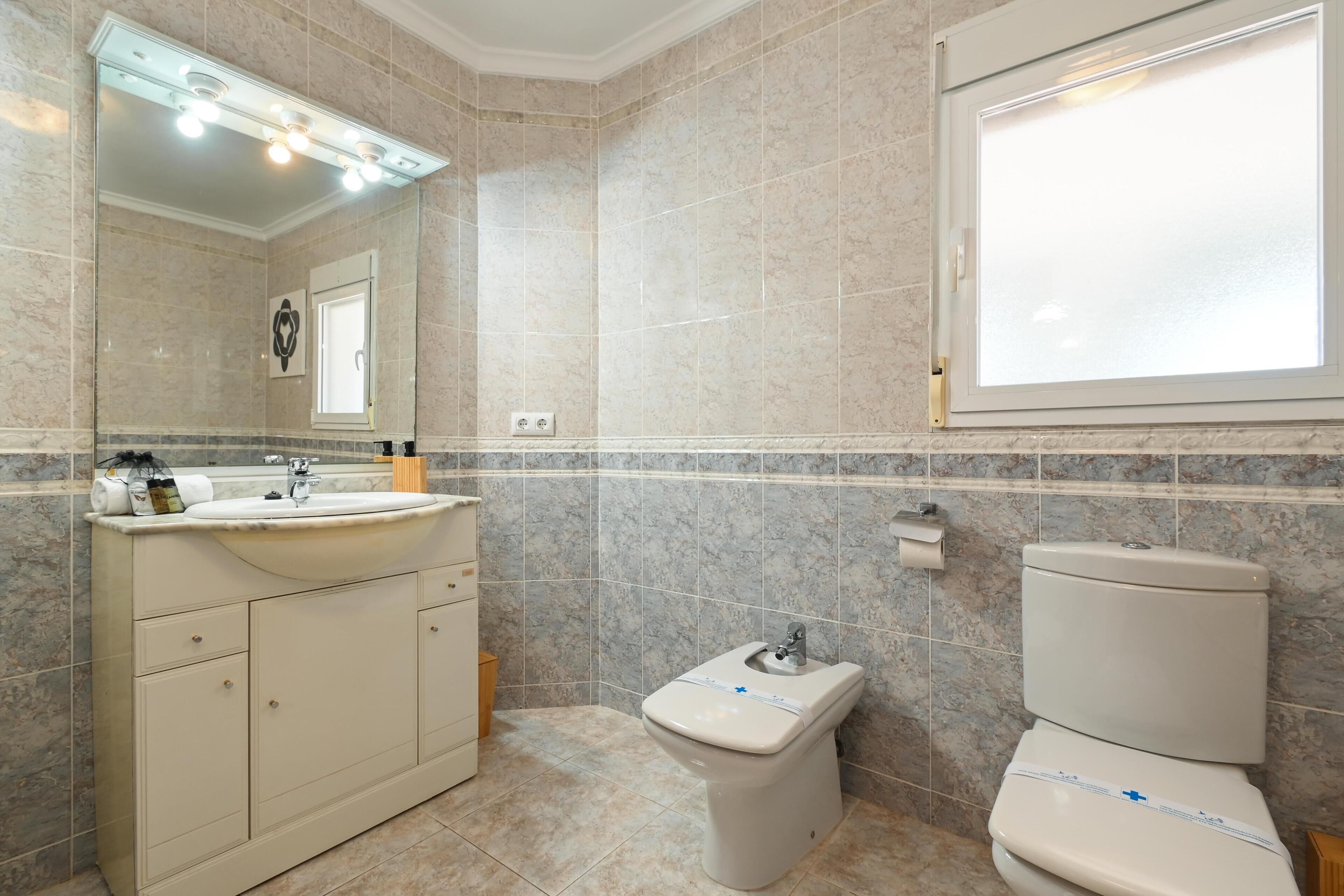 A bathroom with a sink, mirror, toilet, and marble tiles.