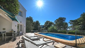 Zona de piscina con sillones reclinables, una mesa y una pileta.