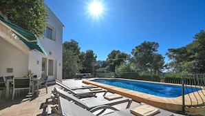 Zona de piscina con sillones reclinables, una mesa y una pileta.