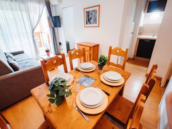 Een eethoek met een houten tafel voor vier personen, stoelen, een kleine plant en een lijst met een foto aan de muur.