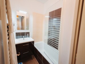 Een moderne badkamer met een wit wastafelmeubel, donkere kastjes, een grote spiegel en een raam met zonwering.