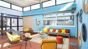 A spacious room with a large window, a sofa with colorful cushions, and a yellow chair. - House in Leucate by Beach & Lagoon (Leucate)