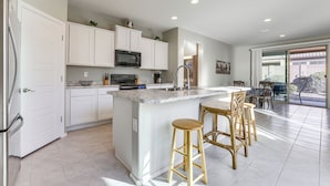 Een moderne keuken met witte kasten, een centraal eiland met krukken, een magnetron en een spoelbak.
