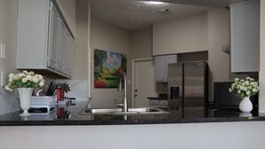 A modern kitchen with white cabinets, a stainless steel refrigerator, and a sink. There are two stools at the counter. - Peaceful Retreat  Near NASA & Kemah 3BR/2BA (Houston)
