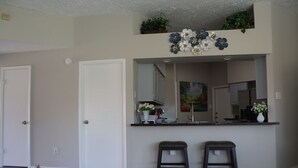 A modern kitchen with a central island, two bar stools, and a decorative flower arrangement above the island. - Peaceful Retreat  Near NASA & Kemah 3BR/2BA (Houston)