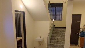 Un vaste espace de vie avec un escalier menant à l’étage supérieur. On aperçoit un évier près de l’escalier, et une porte est visible au fond.