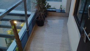 Un balcon agrémenté de plantes en pot, une vue sur les immeubles et une rambarde en verre.
