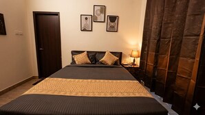 Un lit bien fait, recouvert d’une couvre-lit à motifs, une table de chevet avec une lampe, et une porte sur le côté gauche.