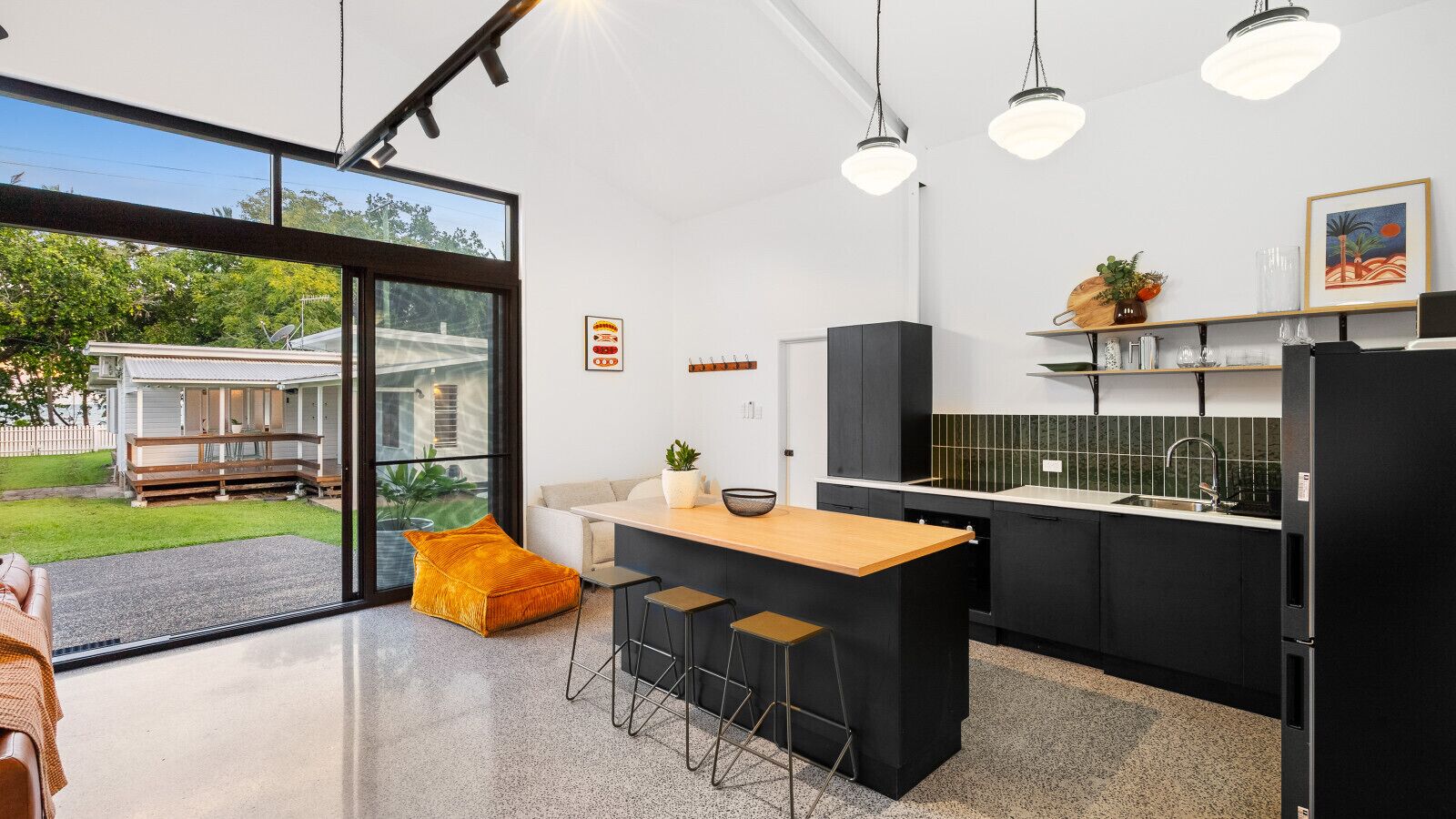 Une cuisine moderne dotée d’un îlot central, de meubles de couleur noire et d’une grande fenêtre donnant sur une maison.