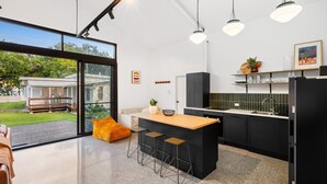 Una cocina moderna con una isla central, armarios negros y un amplio ventanal con vista a una casa.