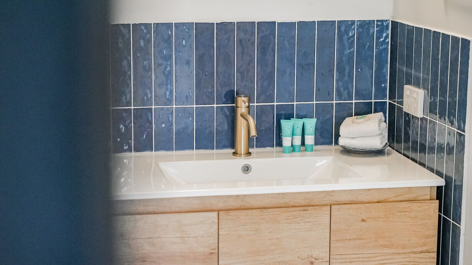 A bathroom with a white sink, a gold faucet, and blue tiles on the wall.