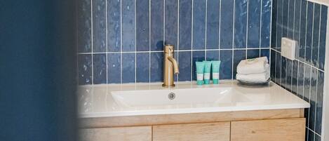 A bathroom with a white sink, a gold faucet, and blue tiles on the wall.