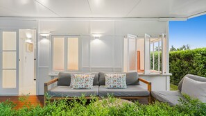 Uma sala de estar moderna com um sofá cinzento, duas almofadas estampadas e vista para um jardim exuberante através de grandes janelas.