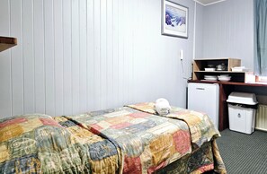 A small, neatly arranged hotel room with a bed, a small desk with a computer, and a radiator. - Room 04 : Inviting Studio Sleeps 3 | Near Shops (Jindabyne)