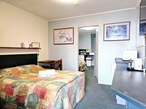 A hotel room with a bed, a desk, a chair, a coffee maker, and framed pictures on the wall. - Room 04 : Inviting Studio Sleeps 3 | Near Shops (Jindabyne)