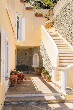 A narrow, sunlit courtyard with a stone wall, a white staircase, and potted plants. - Villa Uma: A bright and sunny two-story villa which faces the sun and the sea, with Free WI-FI. (Praiano)