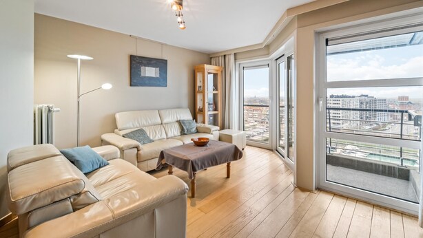 A modern living room with a leather sofa, a coffee table, and a floor lamp. There is a large window offering a city view. - Cozy four bedroom apartment by the harbor (Blankenberge)