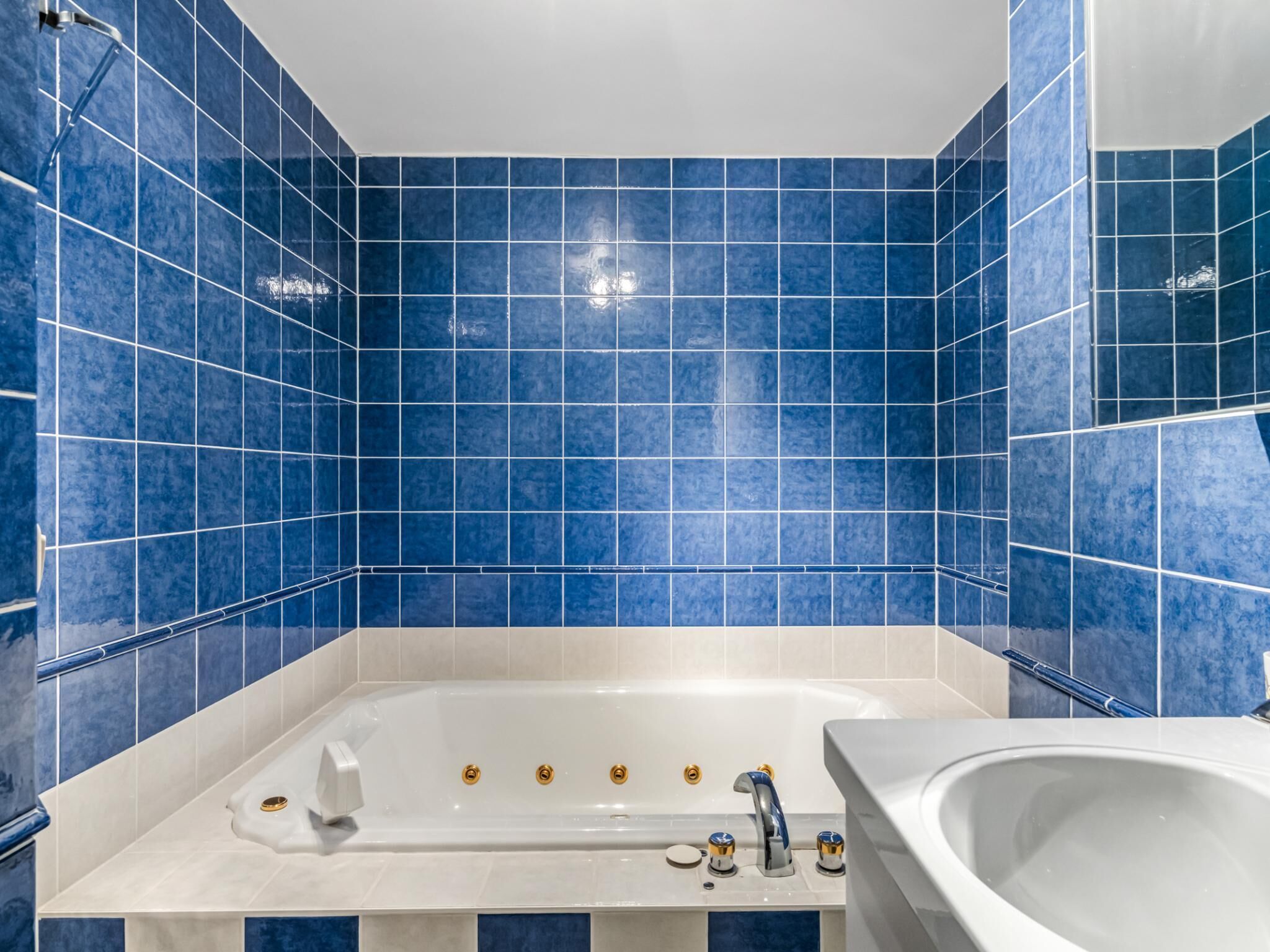 Ein Badezimmer mit blauen Fliesen, einer Badewanne, einem Waschbecken und einer Dusche.