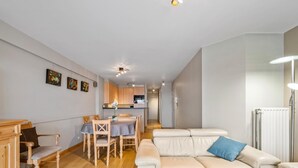 A modern living room with a sofa, a dining table, and a kitchen in the background. - Cozy four bedroom apartment by the harbor (Blankenberge)