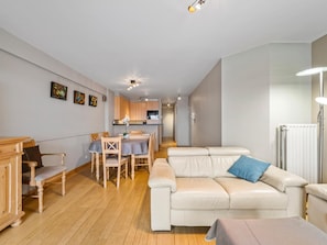 A modern living room with a sofa, a dining table, and a kitchen in the background. - Cozy four bedroom apartment by the harbor (Blankenberge)