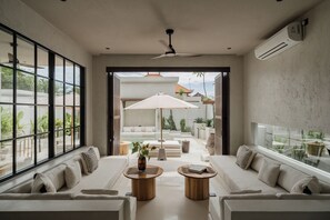 A modern living room with a sofa, coffee table, and a view of the outdoor patio. - Heritage Villas (Pecatu)