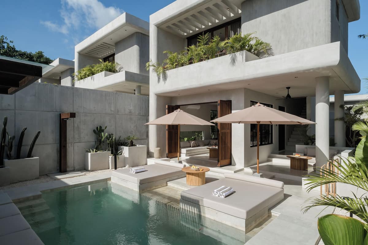 A modern poolside area with concrete architecture, outdoor seating, and greenery.