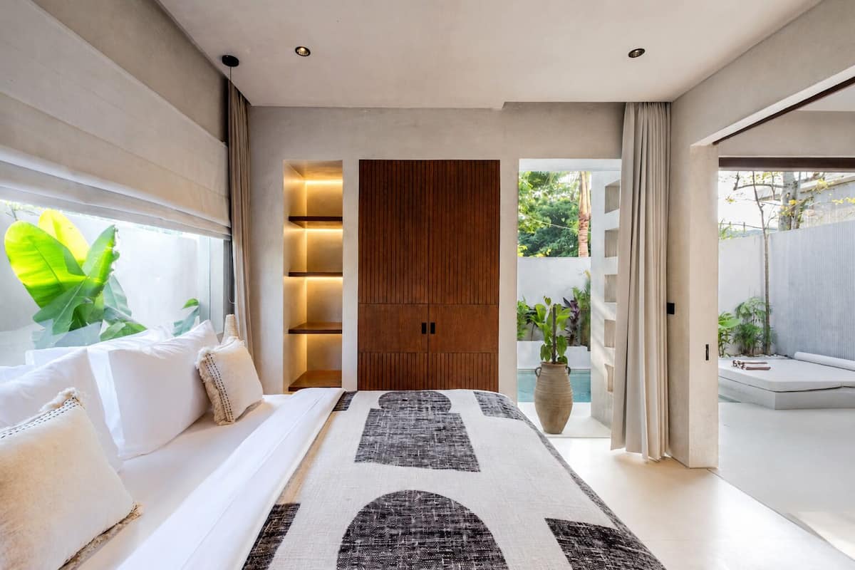 A modern bedroom with a large bed, a wooden wardrobe, and a view of a garden.