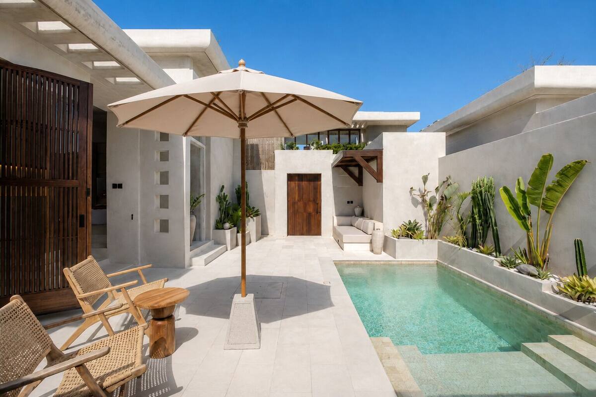 A modern outdoor pool area with a wooden bench and umbrella, surrounded by plants and a concrete wall.