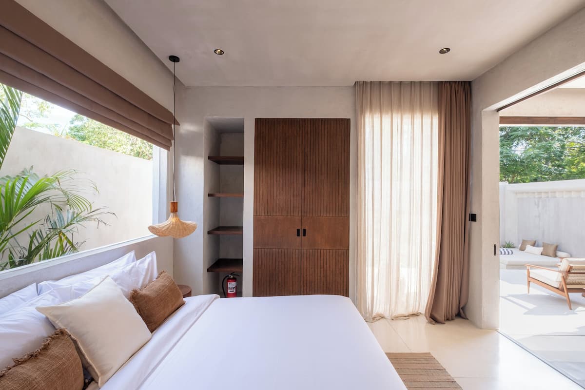 A modern bedroom with a large bed, wooden wardrobe, and a view of an outdoor seating area.