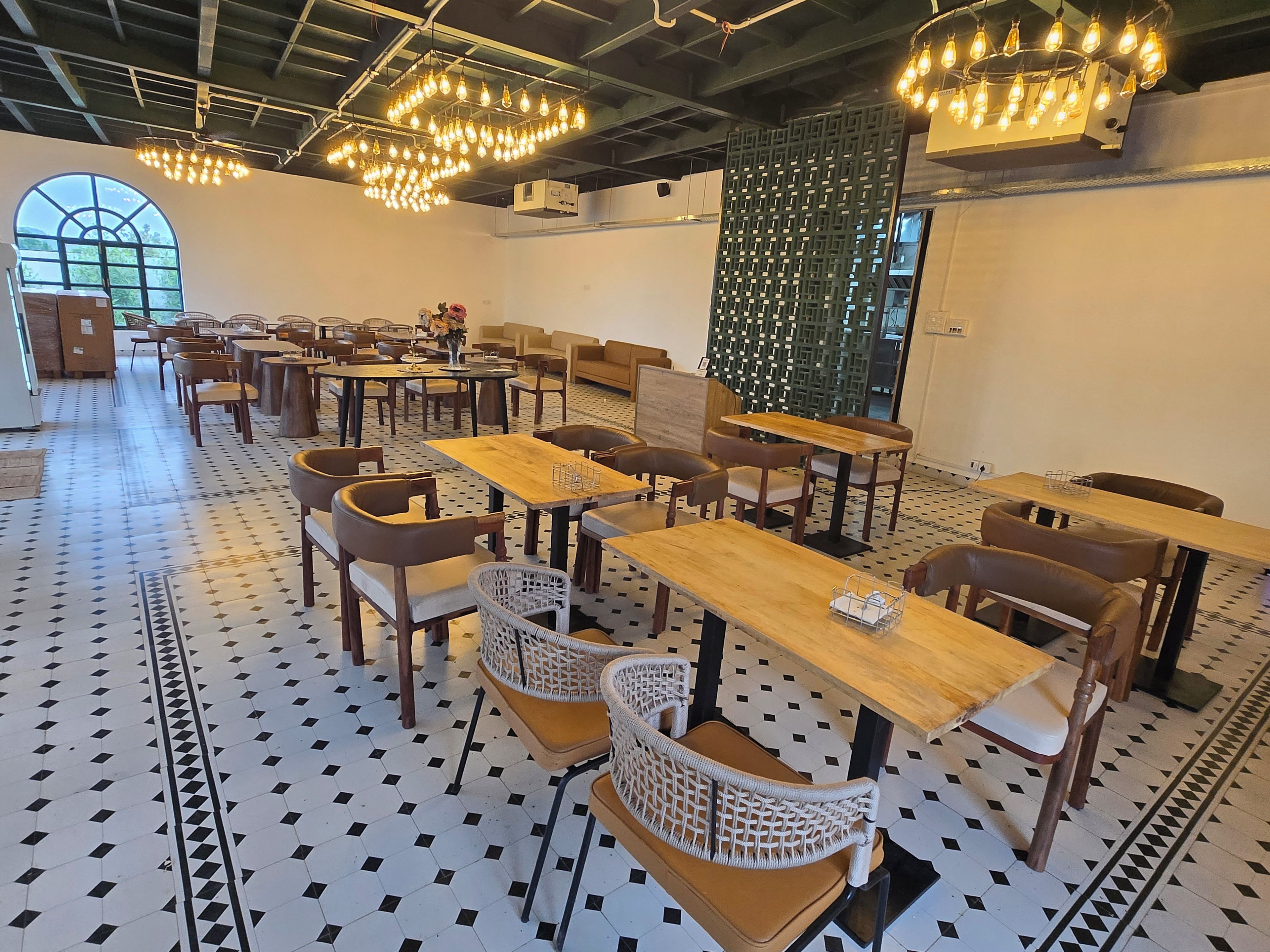 A spacious indoor area with multiple tables and chairs, a patterned floor, and hanging light fixtures.