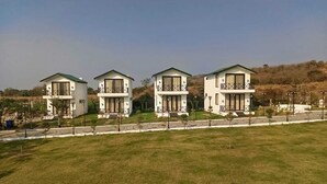 Une rangée de trois maisons à deux étages, dotées de balcons, se dresse sur un terrain herbeux sous un ciel dégagé.