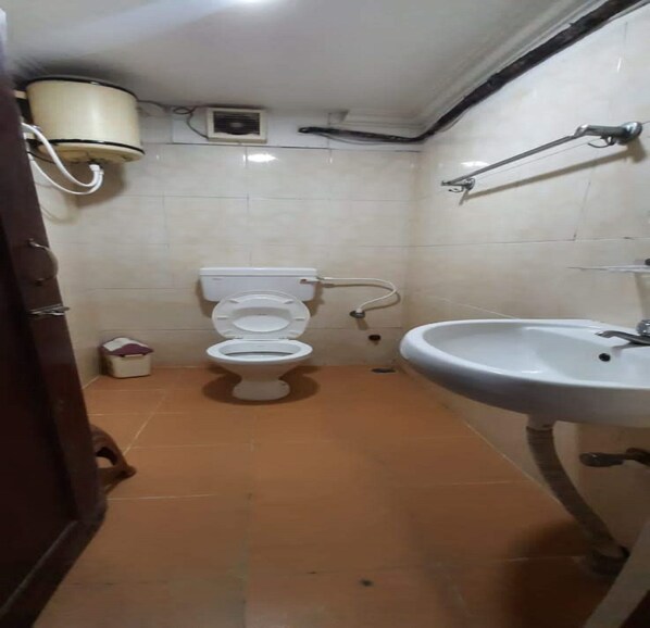 A small bathroom with a toilet, a sink, and a shower. - Ajantha Guest House (Puducherry)