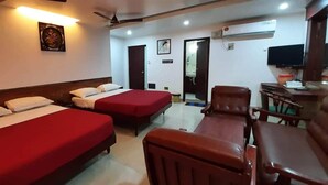 A hotel room with two beds, a desk, a chair, a television, and a ceiling fan. - Ajantha Guest House (Puducherry)