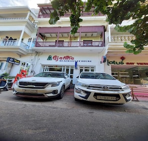 A two-story building with a sign for 'Ajantha Beach Guest House'. Two white SUVs are parked in front.