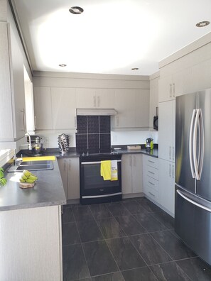 A modern kitchen with a central island, stainless steel appliances, and light-colored cabinetry. - Warm and friendly Canadian home 20 minutes from Montreal (Mascouche)