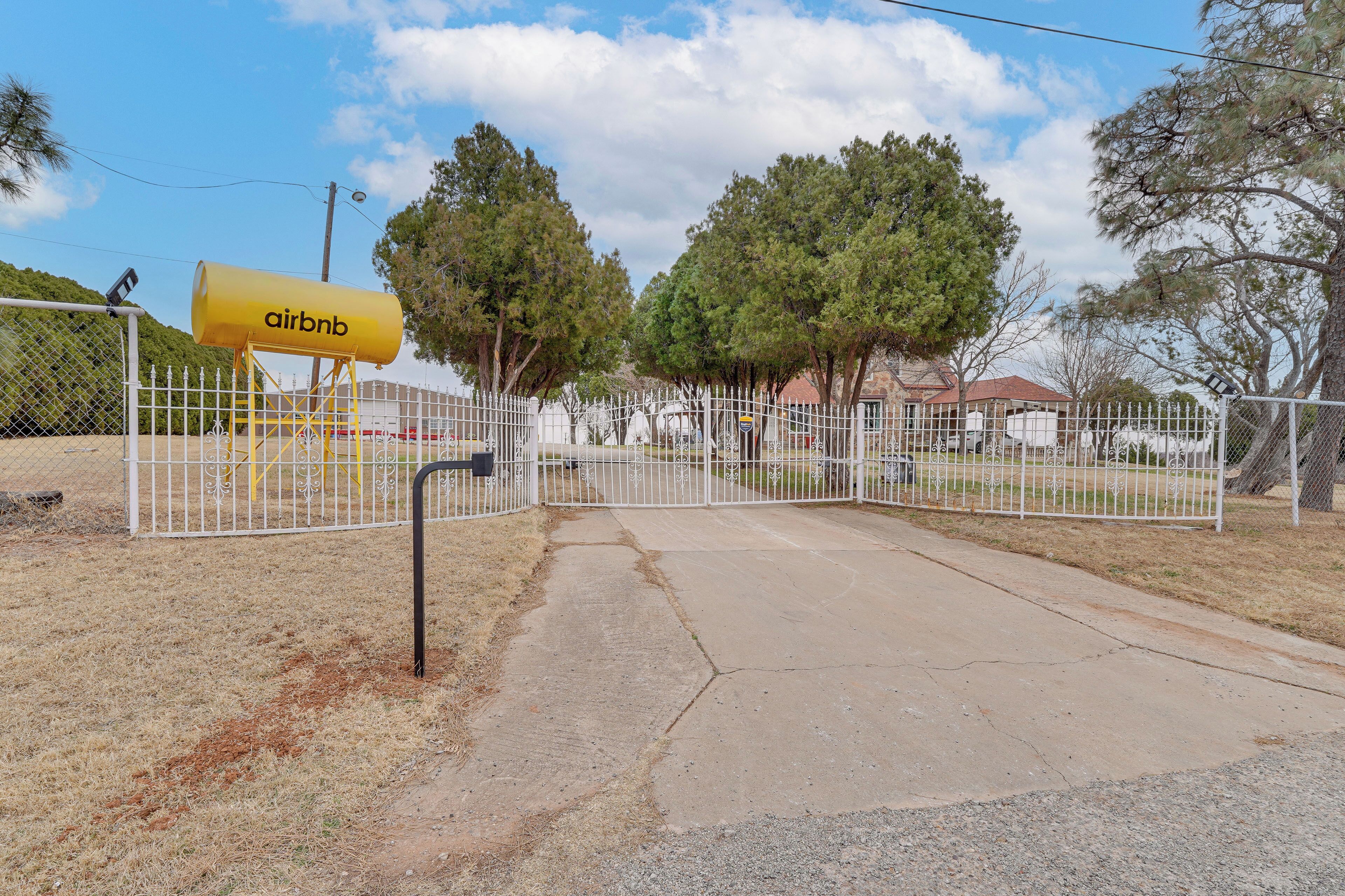 A gated entrance with a yellow Airbnb sign, surrounded by a white fence and trees.