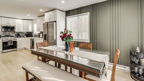 A modern kitchen with white cabinets, stainless steel appliances, and a dining area with a glass table and wooden chairs. - All-Season Fun! Tobyhanna Getaway w/ Lake Access (Tobyhanna)