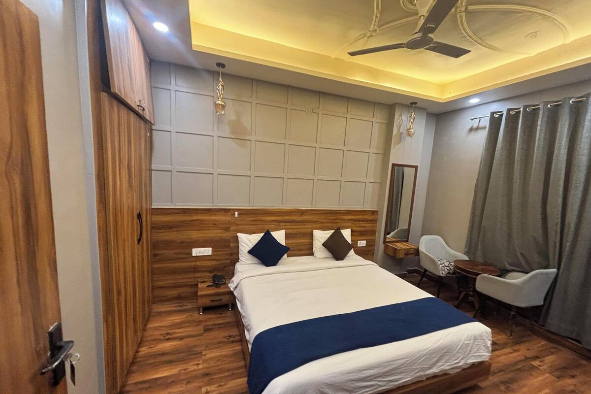 Una habitación de hotel con una cama de madera, un escritorio, una silla, un espejo y un ventilador de techo.