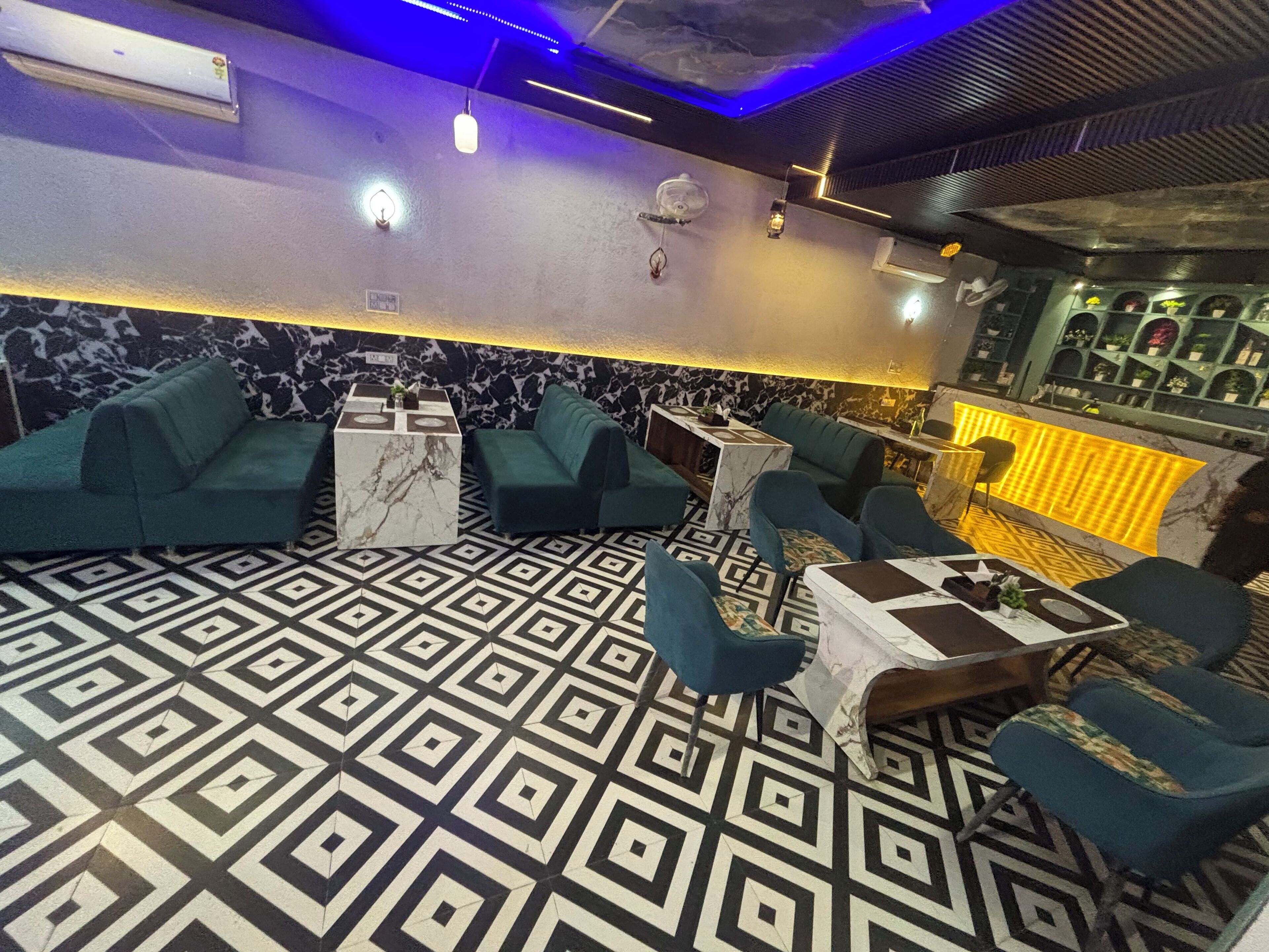 A bar area with green sofas, marble tables, and patterned flooring.