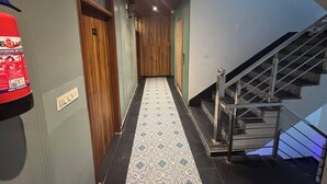 Un couloir avec un tapis à motifs, un extincteur, un panneau indiquant le premier étage et un escalier avec des rampes en métal.